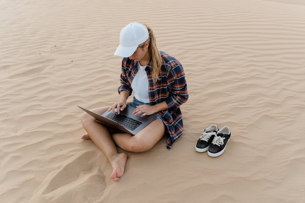 Young woman working with laptop in desert sands, casual attire and remote work concept.